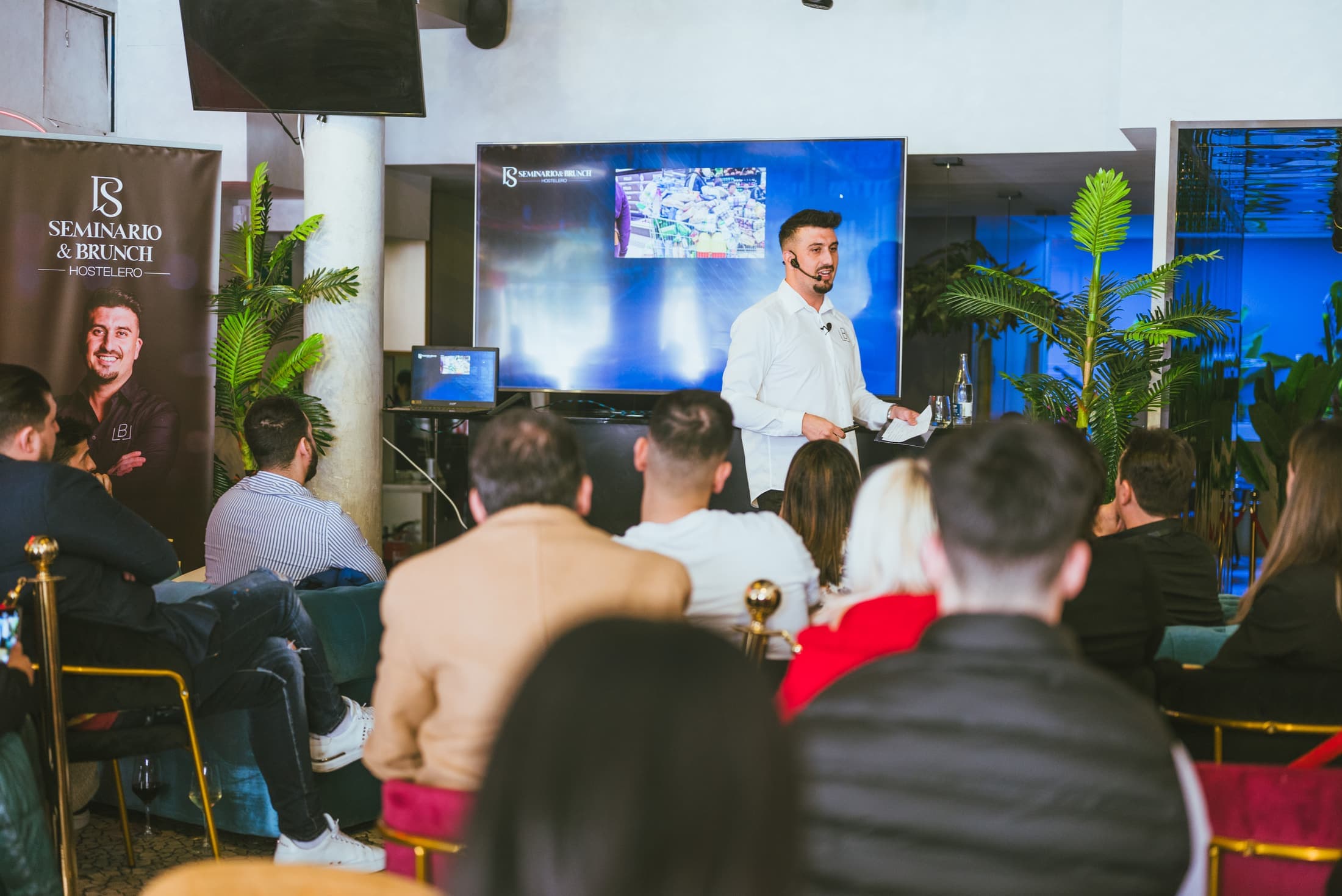 Iván Ballesteros dando clase en un evento presencial, con la sala llena de hosteleros